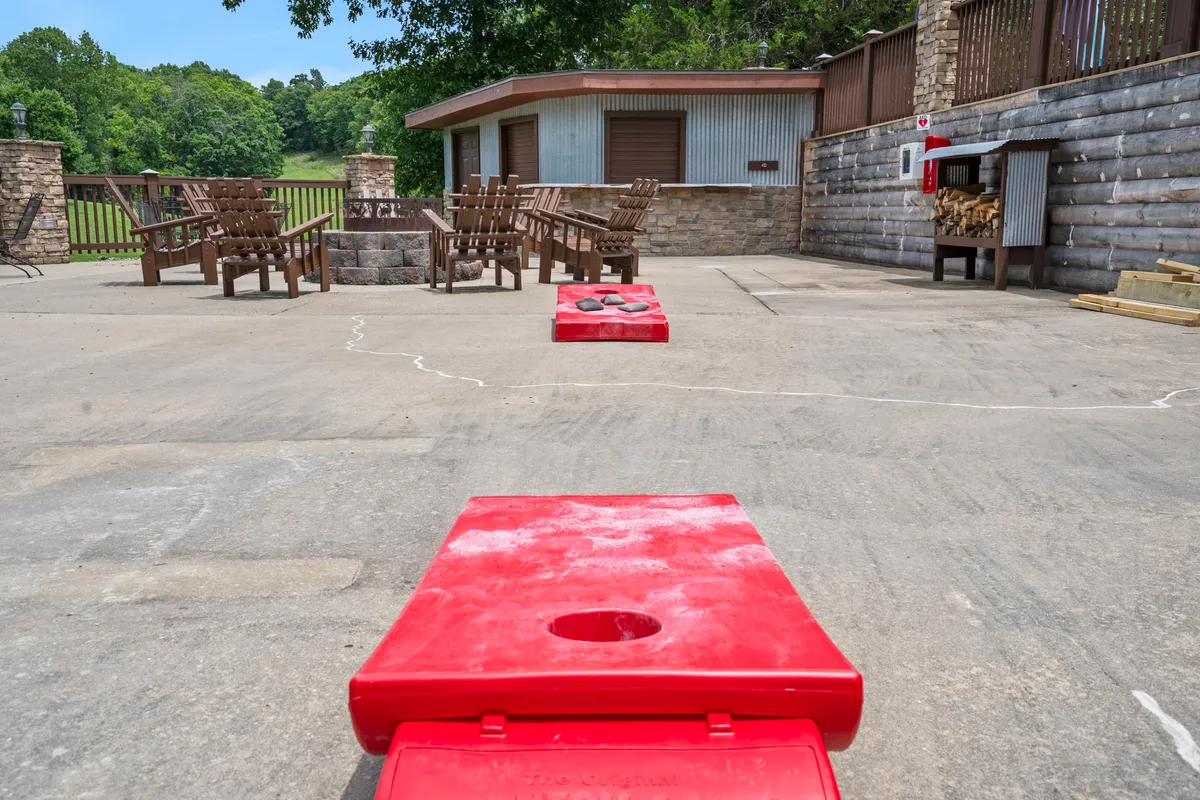 An inviting image of a community fire pit area encircled by wooden chairs, with red cornhole boards nearby. The setting is casual and perfect for evening relaxation and socializing.