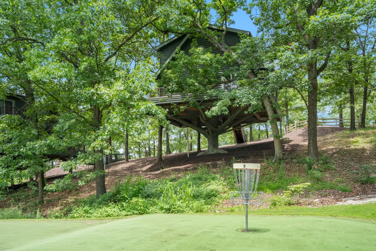 An elevated treehouse and disc golf basket nestled among lush greenery, illustrating the kind of unique outdoor activities and amenities available at the resort. The setting speaks to both adventure and peaceful woodland immersion, with space for gatherings and nature walks.