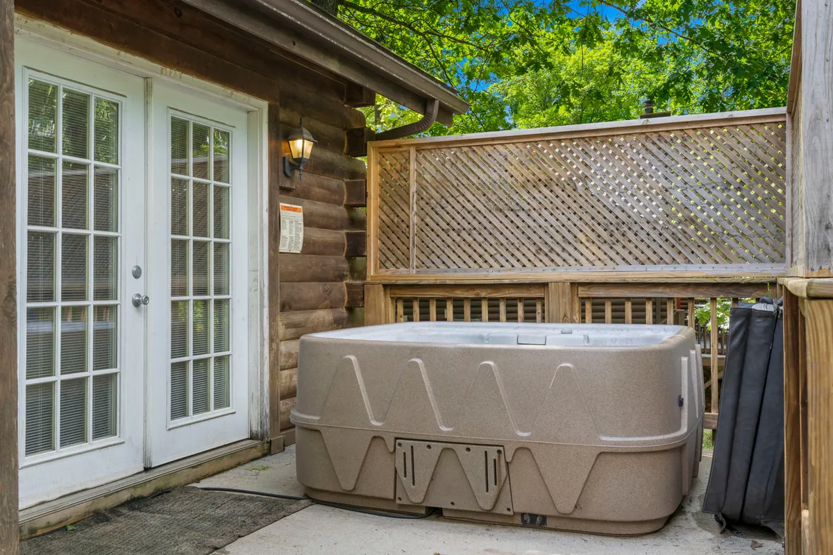 A spacious hot tub sits on a wooden deck near sliding glass doors, offering a tranquil spot to soak with views of the surrounding nature. The setting encourages relaxation and intimate gatherings under the stars.