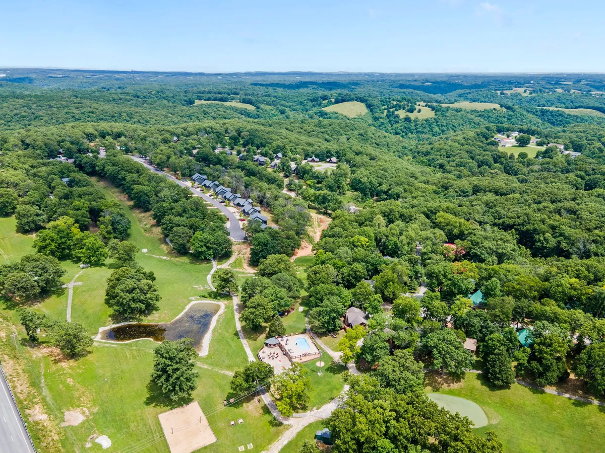 A scenic exterior featuring lush greenery, a serene swimming pool, rolling hills, walking paths, and a small pond, all set in a tranquil Ozarks landscape. The image invites visions of exploring the outdoors, stargazing, and enjoying nature together.