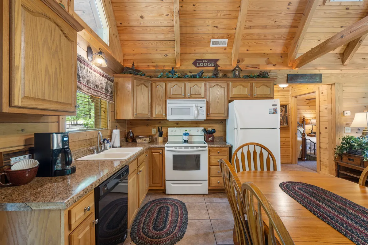 A view of the fully equipped kitchen and adjacent dining table, featuring wooden cabinetry, granite countertops, modern appliances, and attractive table settings. The space feels open and ready for cooking, sharing meals, and entertaining.
