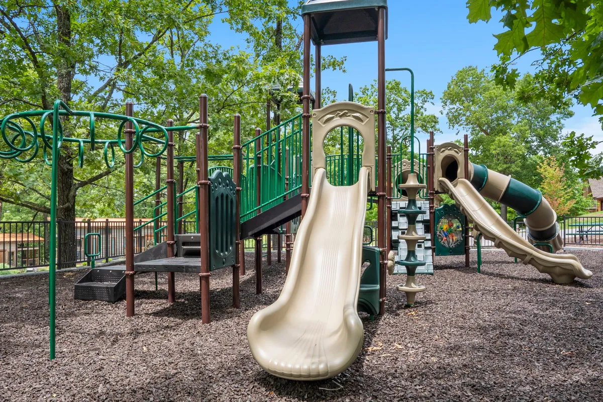 A brightly colored playground featuring slides, a climbing structure, and a swing set, with children playing while parents observe. The area is surrounded by greenery, creating a safe, inviting environment for young guests to explore and enjoy.