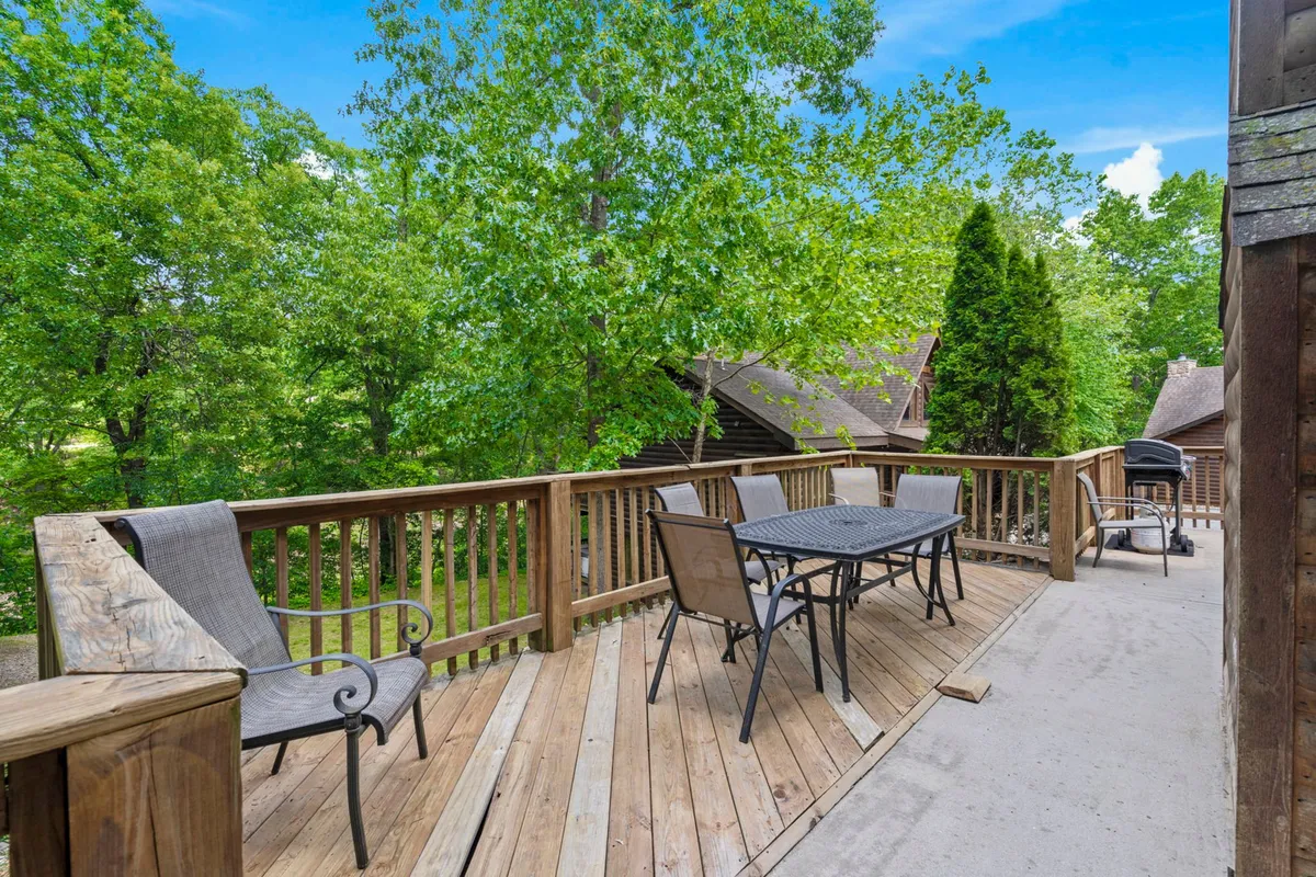 A spacious wooden deck features an outdoor dining table and lounge chairs surrounded by greenery, creating an ideal setting for al fresco meals, sunset views, and socializing. The tranquil backdrop hints at memorable group BBQs or relaxing evenings outdoors.