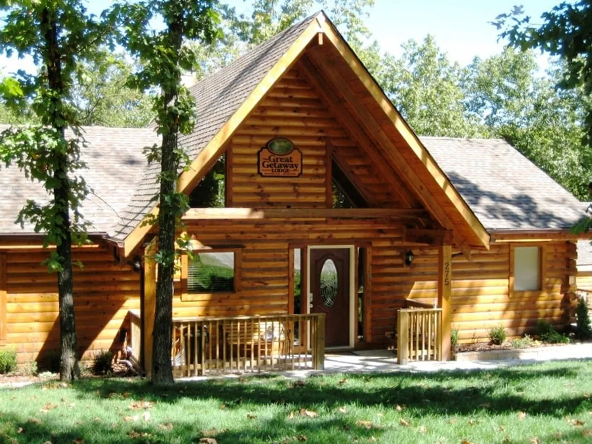A classic log cabin structure with a large front porch and visible signage above the door, surrounded by greenery. The porch invites guests to relax outdoors and soak in the natural setting, evoking a sense of rustic charm and tranquility ideal for a romantic escape.