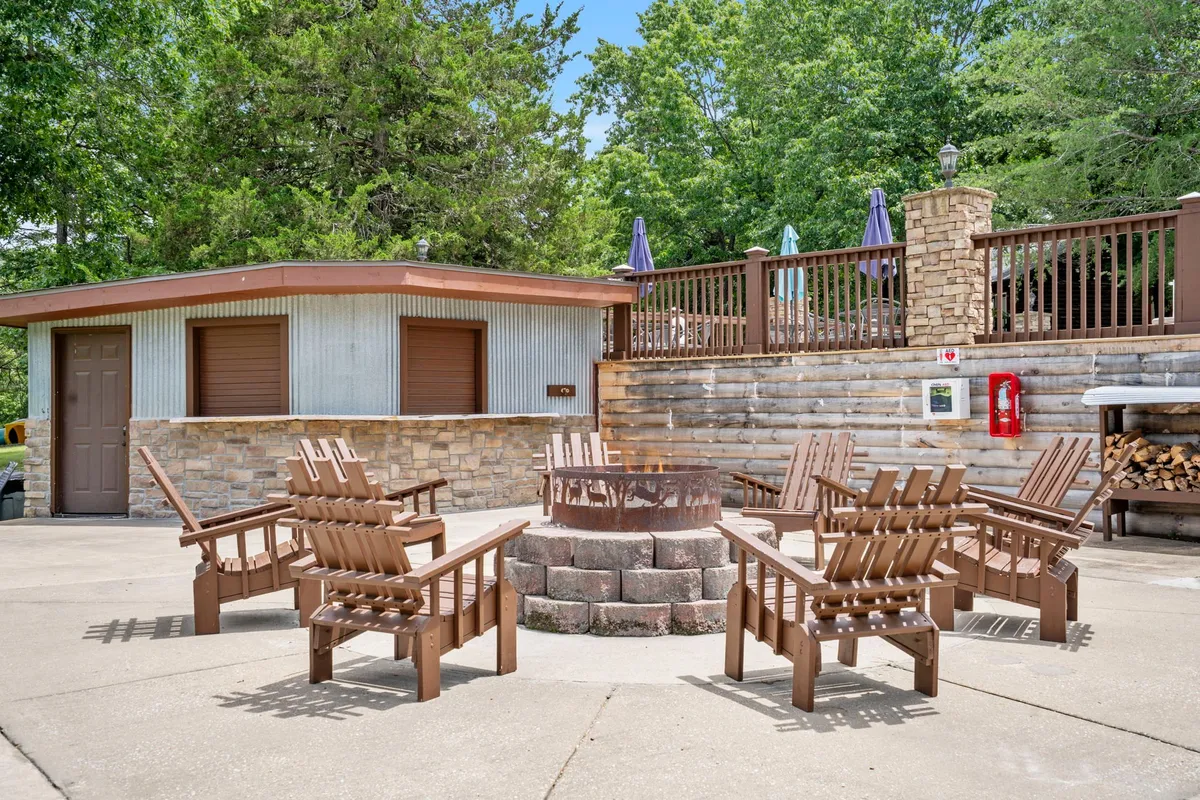 This image features a cozy fire pit area with Adirondack chairs positioned around a stone wall, surrounded by greenery. The setting is ideal for gathering in the evening, roasting marshmallows, and enjoying s’mores under the stars.