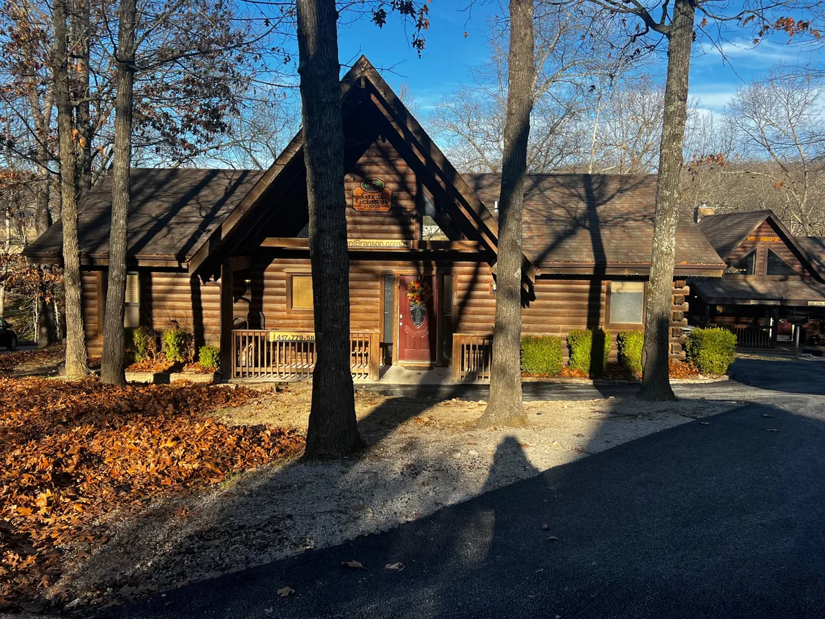 A classic log cabin with a welcoming front porch, adorned with a wreath and surrounded by mature trees. The wood construction and rustic charm are immediately evident from the inviting exterior, with a cozy atmosphere that encapsulates traditional cabin living. The scene hints at the potential for family gatherings and nature-based activities just outside the door.